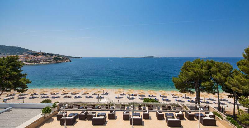 Primošten - pláž před hotelem Zora, slunečníky, lehátka.