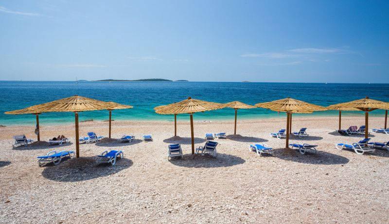 Primošten - pláž před hotelem Zora, slunečníky, lehátka.