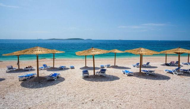 Primošten - pláž před hotelem Zora, slunečníky, lehátka.